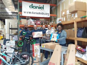 Group of five people holding gifts for children in a warehouse